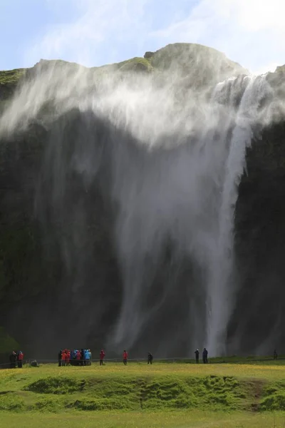 Colpo verticale di persone in piedi vicino alla cascata durante il giorno — Foto Stock