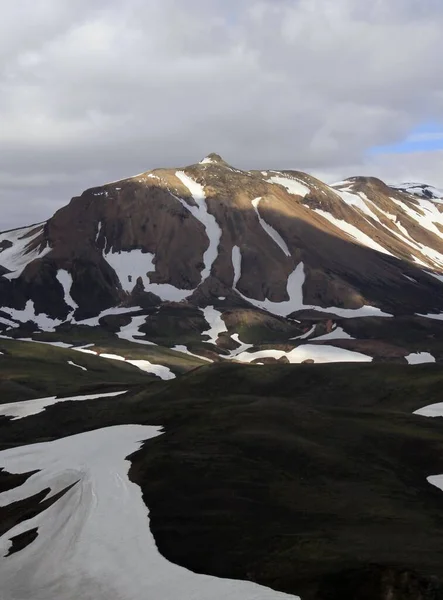 Vertical shot of a mountain covered in snowy patches under a cloudy sky — Stock Photo, Image