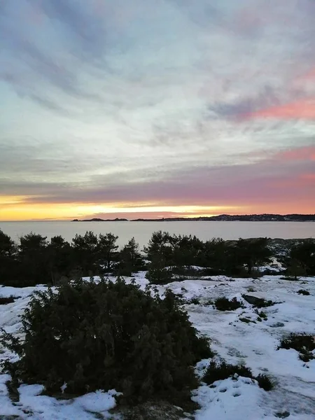 Campo coberto de vegetação e neve cercado pela água sob um céu nublado durante o pôr do sol — Fotografia de Stock