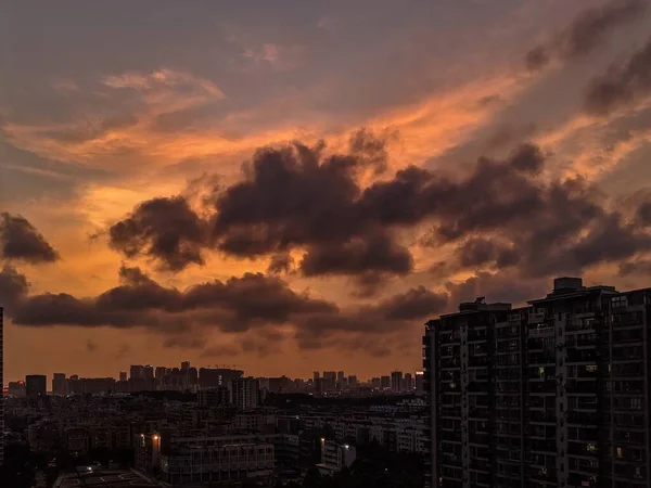 Vue d'ensemble d'une ville moderne et animée avec le ciel orange et les nuages sombres au coucher du soleil — Photo