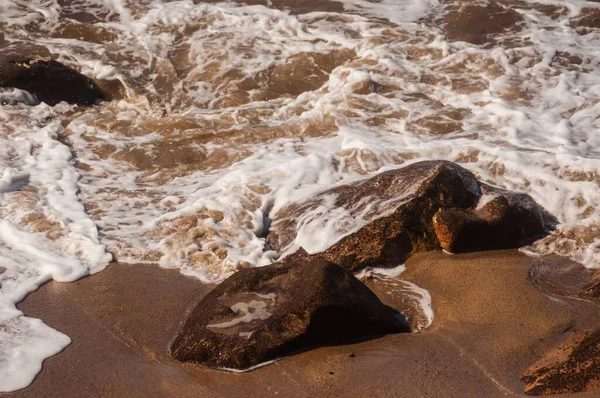 Высокоугольный снимок пенных волн моря, покрывающих камни на берегу — стоковое фото