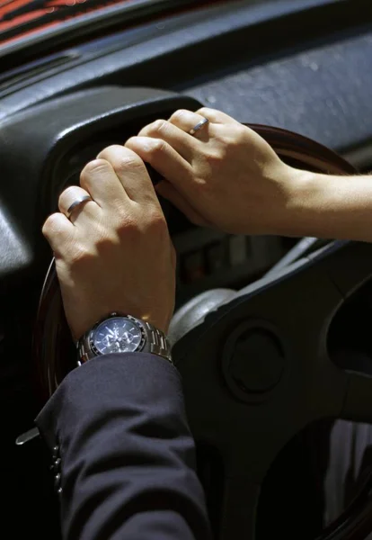 Mãos da noiva e do noivo segurando o volante de um carro juntos — Fotografia de Stock