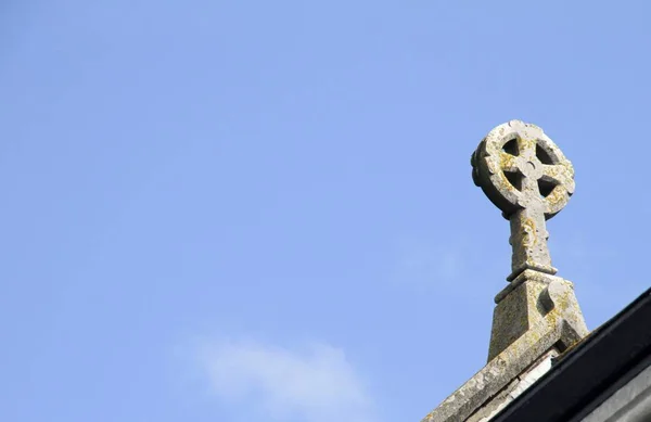 Нижний угол снимка каменного скульптурного креста на вершине церкви с голубым небом на заднем плане — стоковое фото