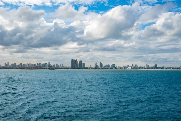 Bred Bild Stadsbyggnader Ett Öppet Hav Med Molnig Blå Himmel — Stockfoto