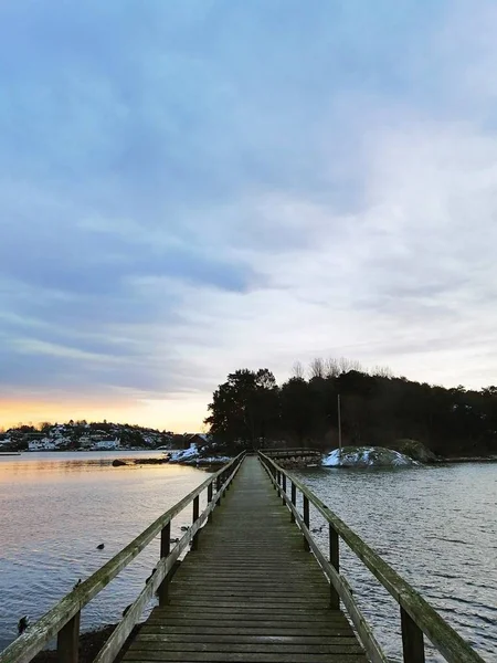 ノルウェーの日没の間、曇った空の下で湖の上の木製の橋の垂直写真 — ストック写真