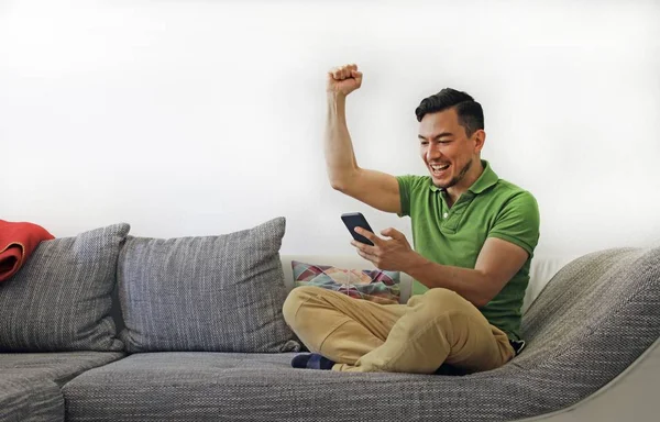 Egy férfi ül a kanapén egy fehér fal mögött, boldogságot és elégedettséget mutatva. — Stock Fotó
