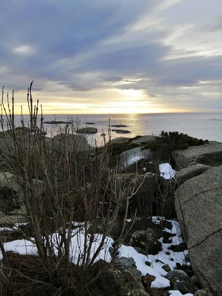 Imágenes verticales de rocas cubiertas de nieve rodeadas por el mar durante la puesta de sol en Noruega. — Foto de Stock