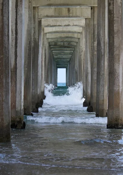 Вертикальний знімок колон мосту над пляжем в оточенні хвиль океану — стокове фото