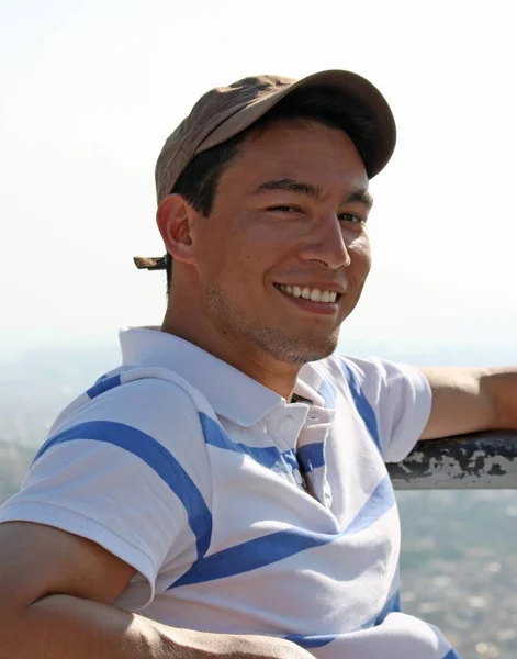 Joven con una gorra marrón sonriendo alegremente con un fondo borroso —  Fotos de Stock