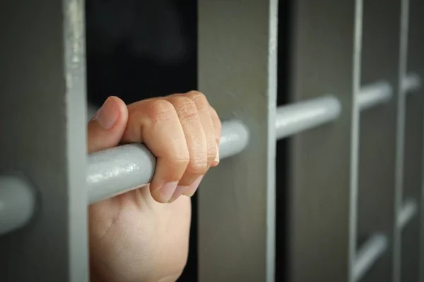 La mano de una mujer sosteniendo las rejas de una celda en una prisión - sin concepto de libertad — Foto de Stock