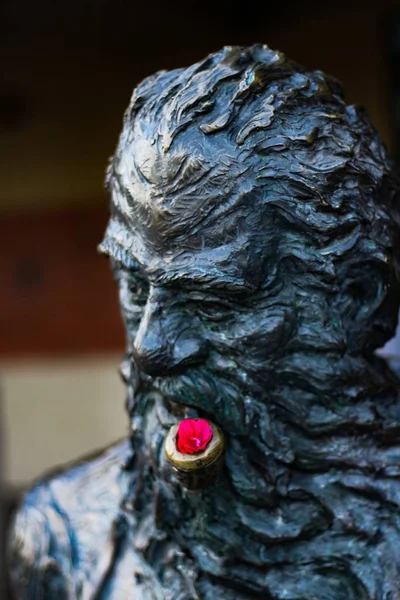 Вертикальный снимок маленького красного цветка на черной каменной скульптуре человека — стоковое фото