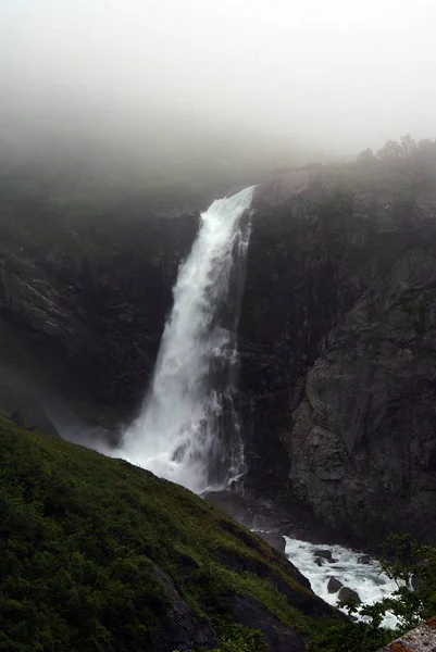 Vertikal bild av ett vackert vattenfall i fjällen omgivet av dimma i Norge — Stockfoto