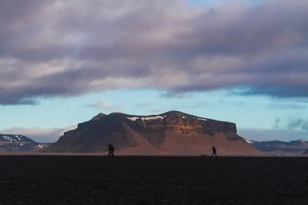 Silhouette of walking people surrounded by rocks covered in the snow under a cloudy sky in Iceland — Stock Photo, Image