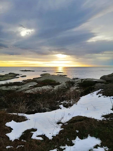 Foto verticale di rocce circondate dal mare sotto un cielo nuvoloso durante il tramonto in Norvegia — Foto Stock