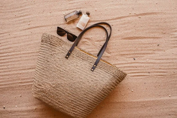 Foto de alto ángulo de la bolsa de una mujer junto al perfume y gafas de sol colocadas en la arena. —  Fotos de Stock