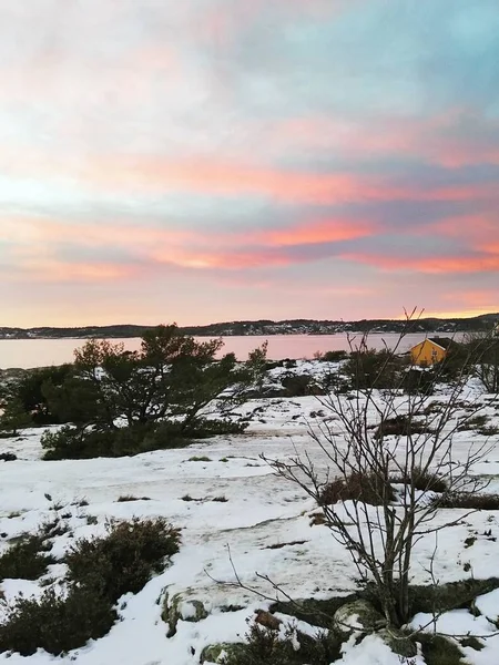 Veld bedekt met groen en sneeuw omgeven door het water onder een bewolkte hemel tijdens de zonsondergang — Stockfoto