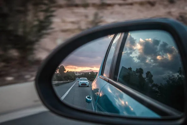 Carretera y coche visto desde el espejo del vehículo delante del mismo. — Foto de Stock