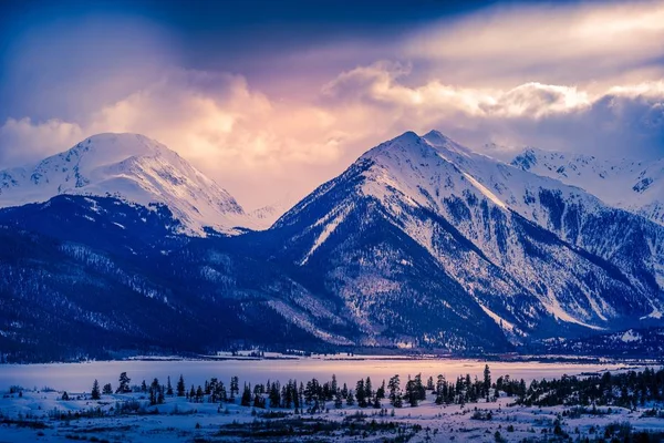 Panoramaaufnahme von schneebedeckten majestätischen Bergen mit einem schwachen Licht von der Sonne — Stockfoto