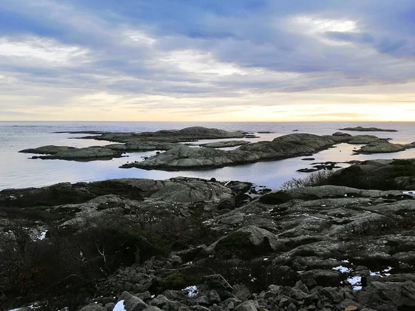 Havet omgivet av klippor täckta av grenar under en molnig himmel under solnedgången i Norge — Stockfoto