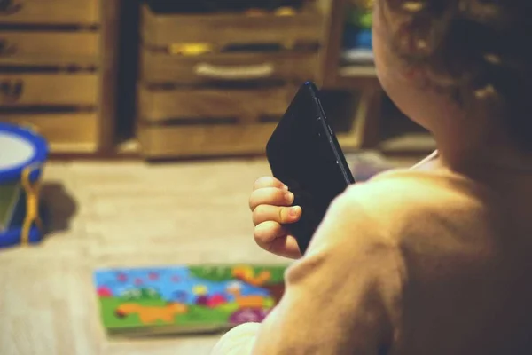 Selektiv fokus skott av ett barn som håller en mobiltelefon enhet med en suddig bakgrund — Stockfoto