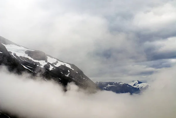 Hermoso paisaje de altas montañas rocosas cubiertas de nieve rodeada de niebla en Noruega. — Foto de Stock