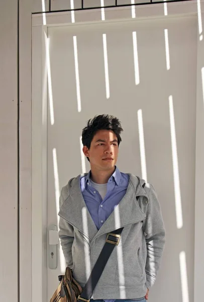 Young man standing near a white door with shadow on him — Stock Photo, Image