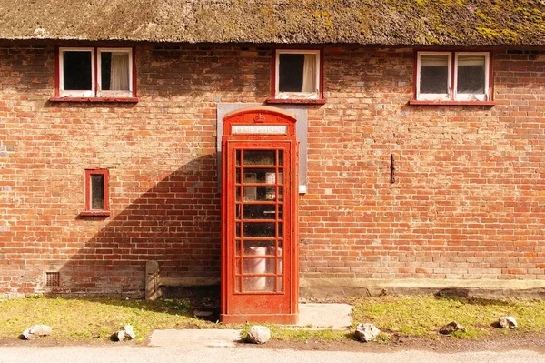Rode telefooncel bij een stenen muur met ramen — Stockfoto