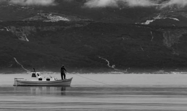 Photo à échelle grise d'un pêcheur à bord d'un bateau dans le lac, avec des montagnes en arrière-plan — Photo