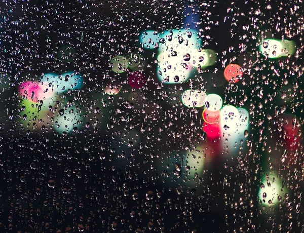 Finestra ricoperta di gocce di pioggia con luci effetto bokeh sullo sfondo sfocato — Foto Stock