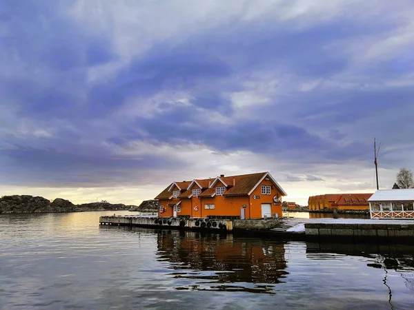 Casa roja rodeada de mar y verdor bajo un cielo nublado durante la puesta de sol en Noruega. — Foto de Stock