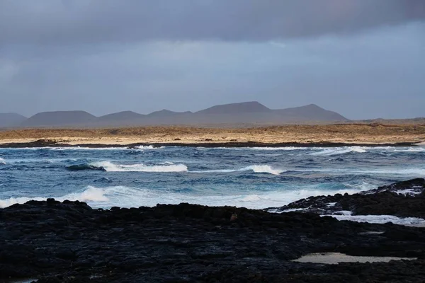 Hermoso tiro de la playa rocosa y de las montañas en el fondo de Fuerteventura, España. — Foto de Stock