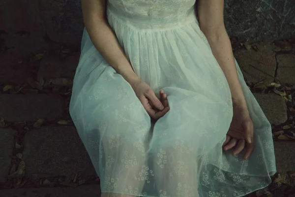 Młoda kobieta w białej sukience siedzi z ręką na kolanach — Zdjęcie stockowe