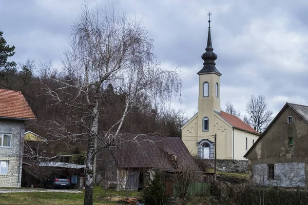 Iglesia rodeada de colinas cubiertas de vegetación y casas bajo un cielo nublado. —  Fotos de Stock