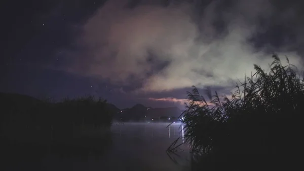 Ночная фотография озера с лучами света на расстоянии и розовыми оттенками в небе — стоковое фото