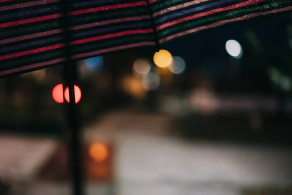 Foto von Nachtlichtern mit Bokeh-Effekt und einem Teil eines überhängenden bunten Regenschirms — Stockfoto