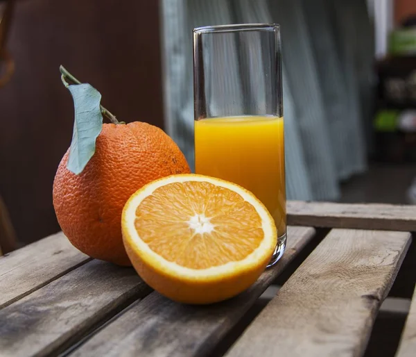 Halb gefülltes Glas Orangensaft und frische Orangen auf einer Holzkiste — Stockfoto