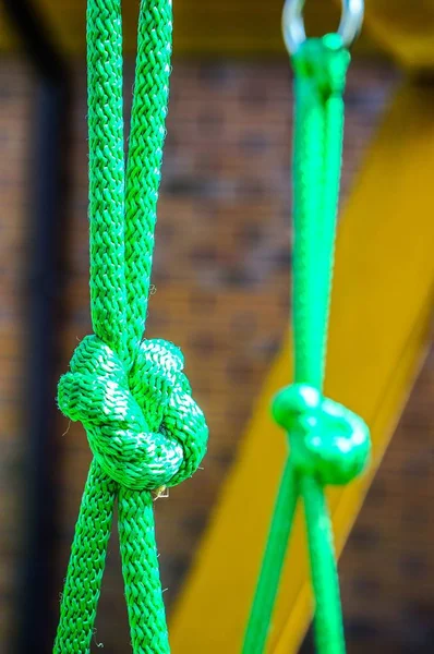 Närbild av ett grönt rep med knutar hängande från metallringar — Stockfoto