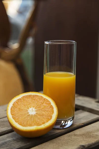 Nahaufnahme eines halb gefüllten Glases Orangensaft und einer in Scheiben geschnittenen Orange auf einer Holzkiste — Stockfoto