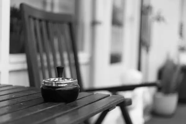 Greyscale tiro de um cinzeiro em uma mesa de madeira com um fundo borrado — Fotografia de Stock