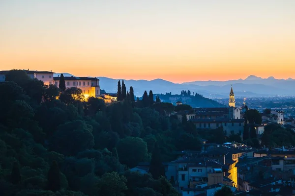 Bellissimo scatto di edifici vicino agli alberi con montagne in lontananza al tramonto — Foto Stock