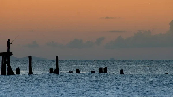 Schöne Silhouette eines Mannes, der in der Abenddämmerung auf den Docks fischt — Stockfoto