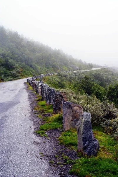 Tiro vertical de uma estrada em uma bela paisagem montanhosa envolta em nevoeiro na Noruega — Fotografia de Stock