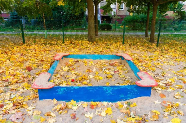 Bonito tiro de um playground de areia no parque coberto por folhas coloridas no outono — Fotografia de Stock