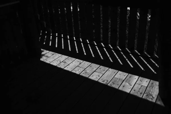 Trä balkong med skuggor av räcken projiceras av eftermiddagssolen i monokrom — Stockfoto