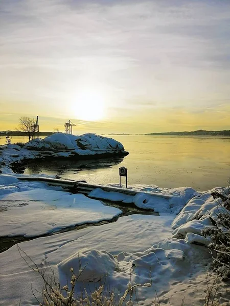 Foto verticale di un'isola coperta dalla neve circondata dal mare durante il tramonto in Norvegia — Foto Stock