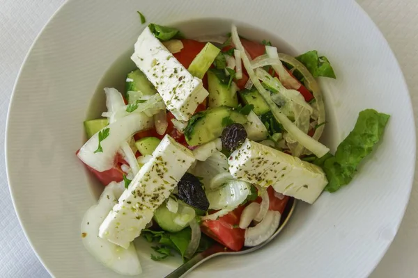 Zbliżenie greckiej sałatki w białej misce pod światłami na białym stole — Zdjęcie stockowe