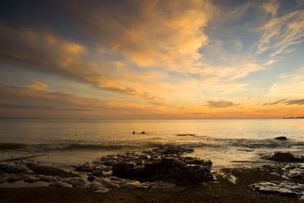 Wide shot of the silhouettes of swimmers by the sea in South Wales during sunset — Stock Photo, Image