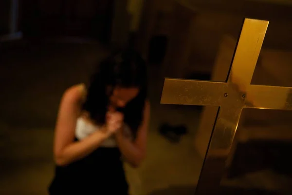 Kątowe ujęcie kobiety modlącej się przed krzyżem w kaplicy — Zdjęcie stockowe
