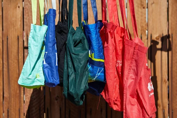 Lote de colorido eco-friendly sacos de pano reutilizáveis pendurados em um poste perto de uma cerca de madeira — Fotografia de Stock