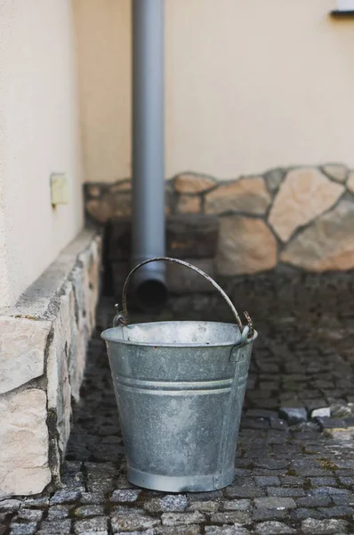 A vertical shot of a metal bucket in the street in front of a building